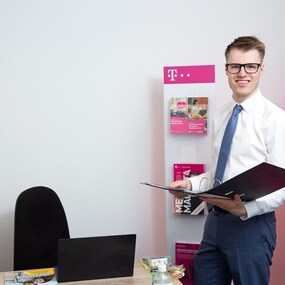 Junger Mann im Telekom Shop mit Anzug und Aktenmappe berät Kunden zu Telekommunikation.